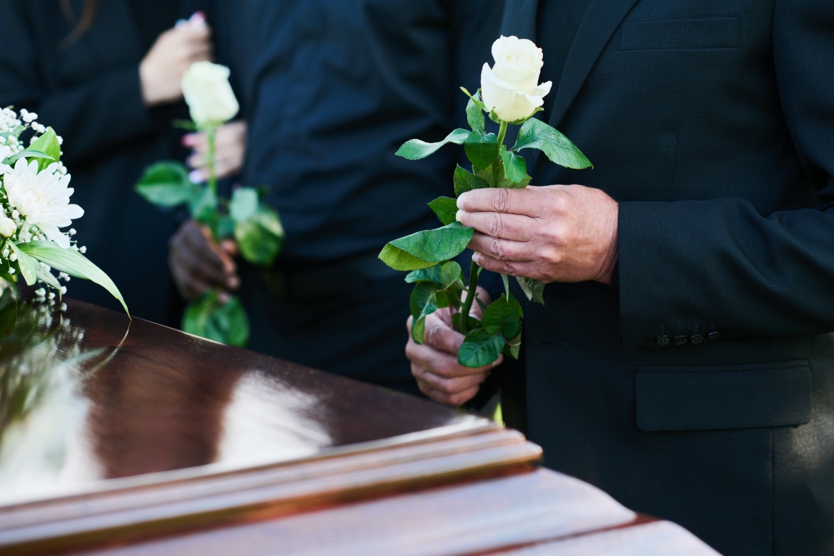Gesto di omaggio: persone davanti al feretro, con di fiori bianchi tra le mani.