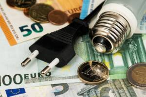 Bollette e risparmio: banconote, spina e lampadina, che richiamano l'elettricità.