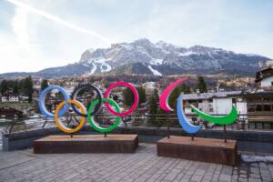 Loghi delle Olimpiadi e Paralimpiadi 2026 con il panorama di Cortina d'Ampezzo sullo sfondo.