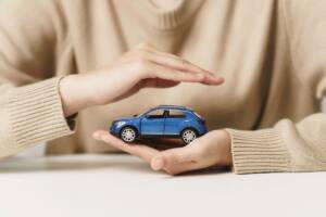Mani che proteggono un modellino di auto, a simboleggiare una polizza assicurativa.