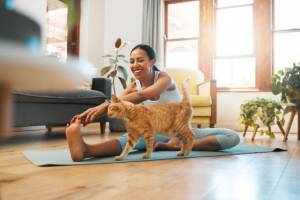 Una ragazza che pratica yoga in salotto accanto al suo gatto rosso.