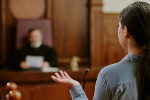 Aula di tribunale con giudice al banco e avvocato durante l'arringa.