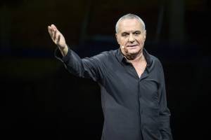 Giorgio Panariello parla durante uno spettacolo con il braccio alzato e vestito di nero
